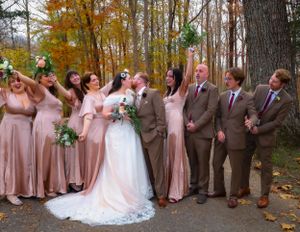 Wedding party in brown suits and pink dresses poses among fall foliage.