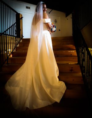 Dramatic lighting illuminates flowing white wedding gown on wooden staircase.