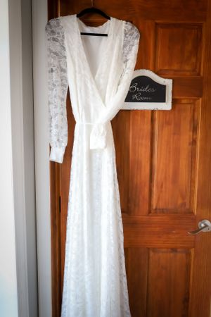 Elegant white lace wedding dress with long sleeves hanging on wooden door.