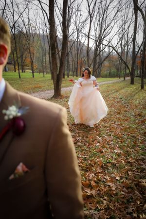 A couple shares a candid moment during their fall wedding photoshoot in a wooded area.