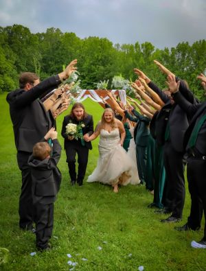 Wedding party forms tunnel with raised arms as couple runs through on grassy lawn during outdoor celebration.