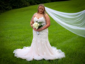 A flowing white lace wedding gown with veil photographed on lush green grass.