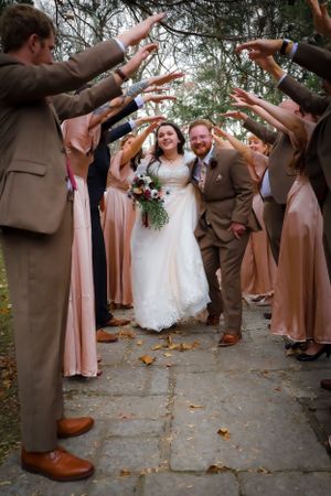 Wedding party forms a tunnel for newlyweds to walk through on autumn path.
