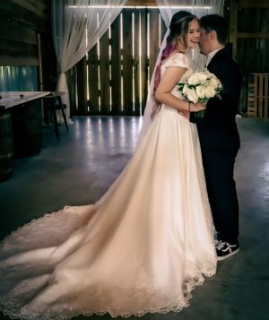 A romantic wedding scene captured in a rustic barn with dramatic lighting and flowing dress train.
