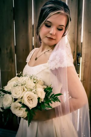 A delicate white rose bouquet held against a white wedding dress with soft lighting.