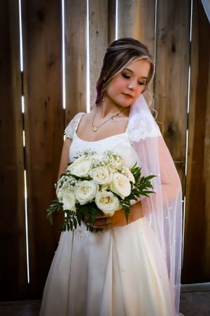 A bride in a white wedding gown holds a beautiful bouquet of white roses and greenery.