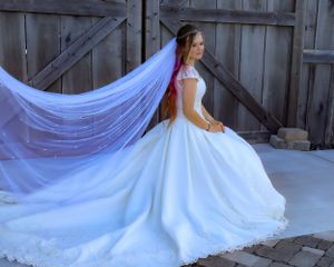 A flowing white wedding dress with a long train spreads across a rustic wooden floor.
