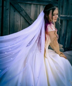 An elegant white wedding gown with flowing veil photographed in dramatic lighting.