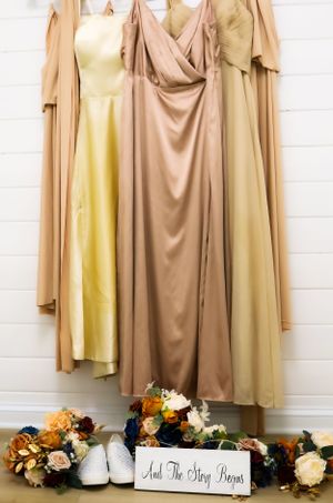 Bridesmaid dresses in neutral champagne tones hanging with floral decorations.