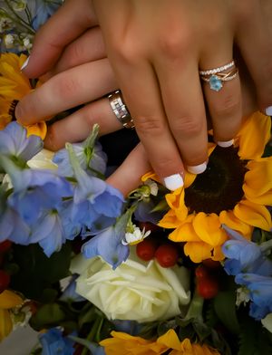 Wedding rings displayed with sunflowers and blue delphinium flowers in romantic detail shot.