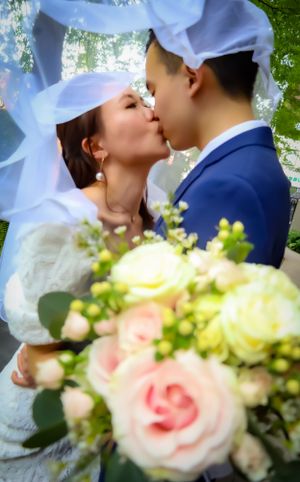 Romantic wedding kiss captured with soft focus and beautiful floral bouquet in foreground.