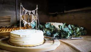 Simple white wedding cake decorated with bunting and greenery on a rustic table.