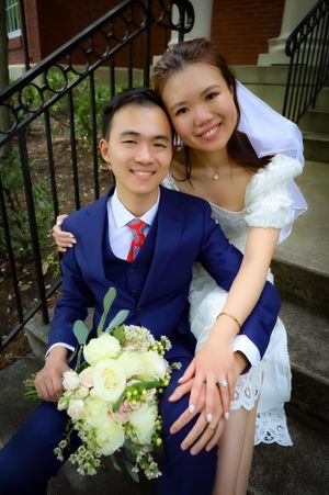 Happy newlyweds pose on brick steps with elegant floral bouquet.
