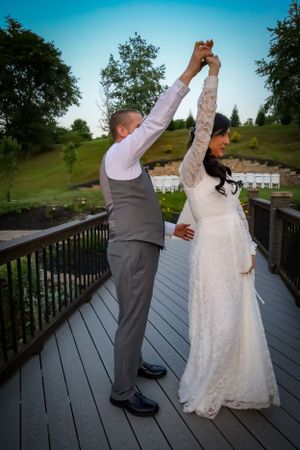 A couple dances together on a wooden deck with blue sky in the background during their wedding celebration.