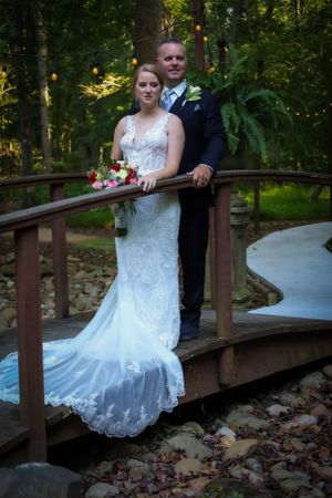 Bride and groom pose together on wooden bridge in outdoor forest setting.