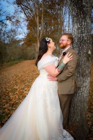 A romantic autumn wedding photoshoot with a couple embracing near trees with fallen leaves.