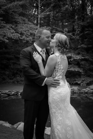 Black and white portrait of couple embracing by waterside during wedding.