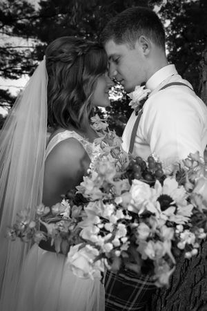 Intimate black and white portrait of newlyweds sharing a tender moment with floral bouquet.