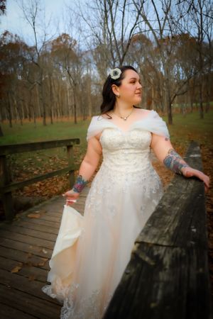 A bride in a sparkly white dress poses on a wooden boardwalk surrounded by fall foliage.