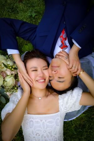 Creative overhead shot of newlyweds lying on grass with bouquet.