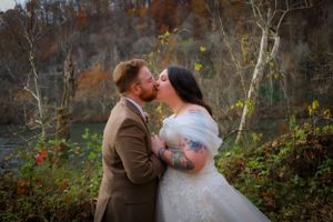 A couple shares a tender kiss during their autumn outdoor wedding ceremony.