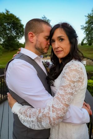 A romantic couple embraces on a deck during a wedding photoshoot, with the bride wearing a white lace dress.
