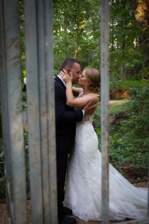 Artistic wedding photos of a couple embracing between tall tree trunks in a wooded area.