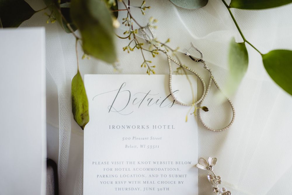 Close-up of delicate wedding invitation with calligraphy and silver jewelry accents.