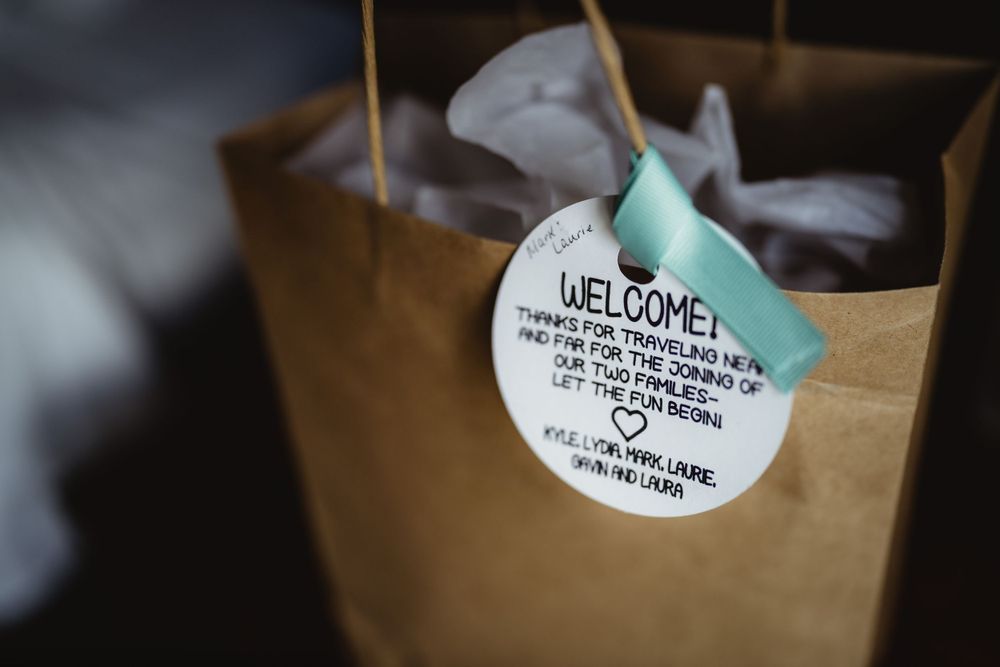 Welcome tag with blue ribbon attached to brown paper gift bag.