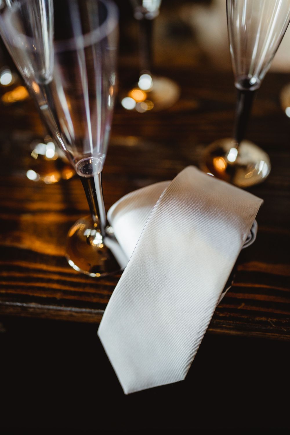 White necktie lying on dark wood table with champagne flutes.