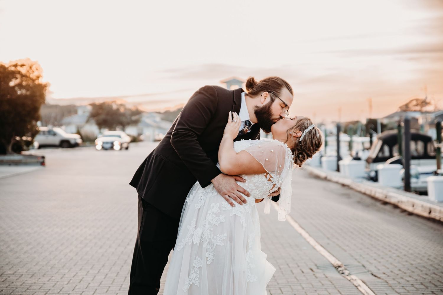 Romantic sunset portrait of newlyweds sharing a kiss on a marina dock.