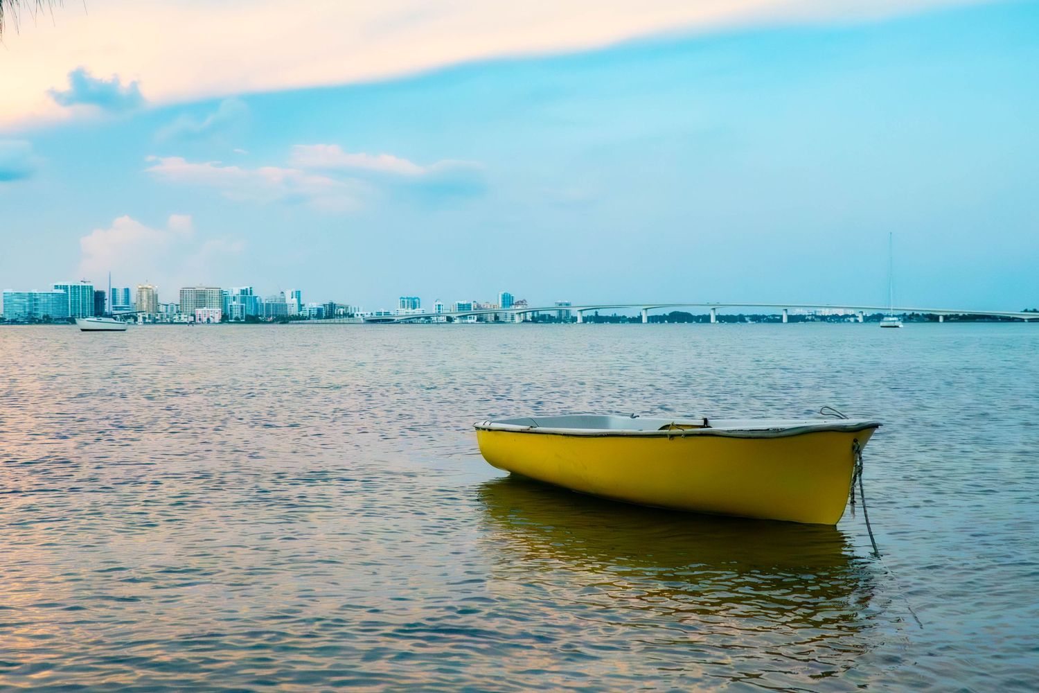 A yellow boat floats on calm waters with a city skyline in the distance.