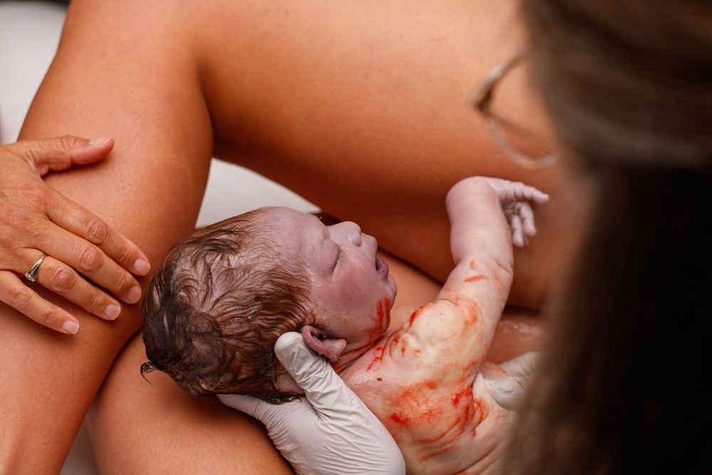 Healthcare provider holding newborn baby immediately after birth showing vernix on skin.