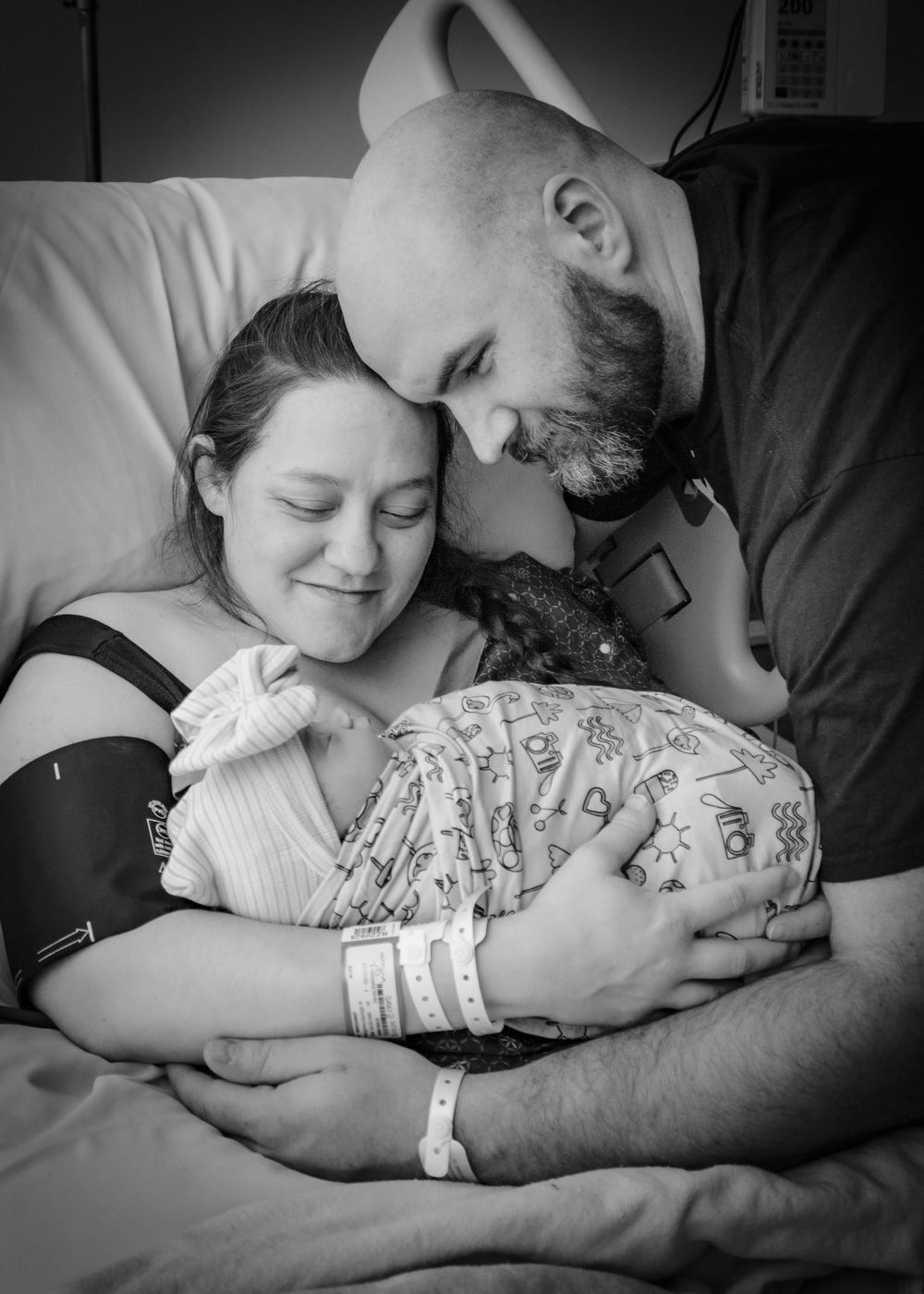 Black and white photo of intimate moments after birth as new parents hold their swaddled newborn.