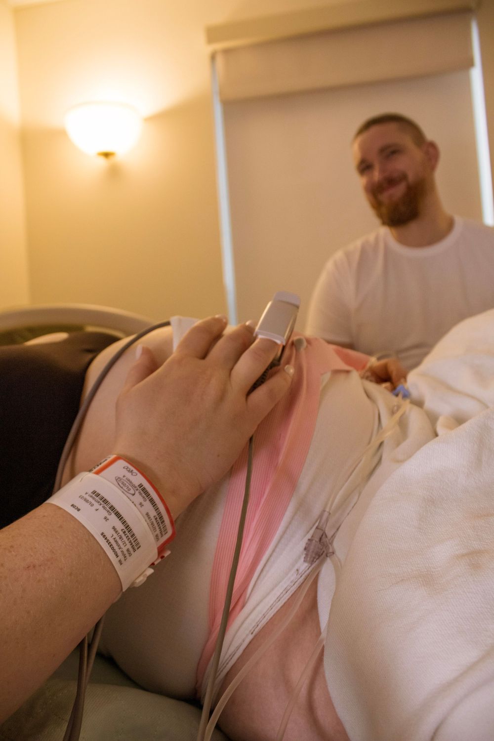 Hospital patient with wristband holding mobile device while resting in bed.