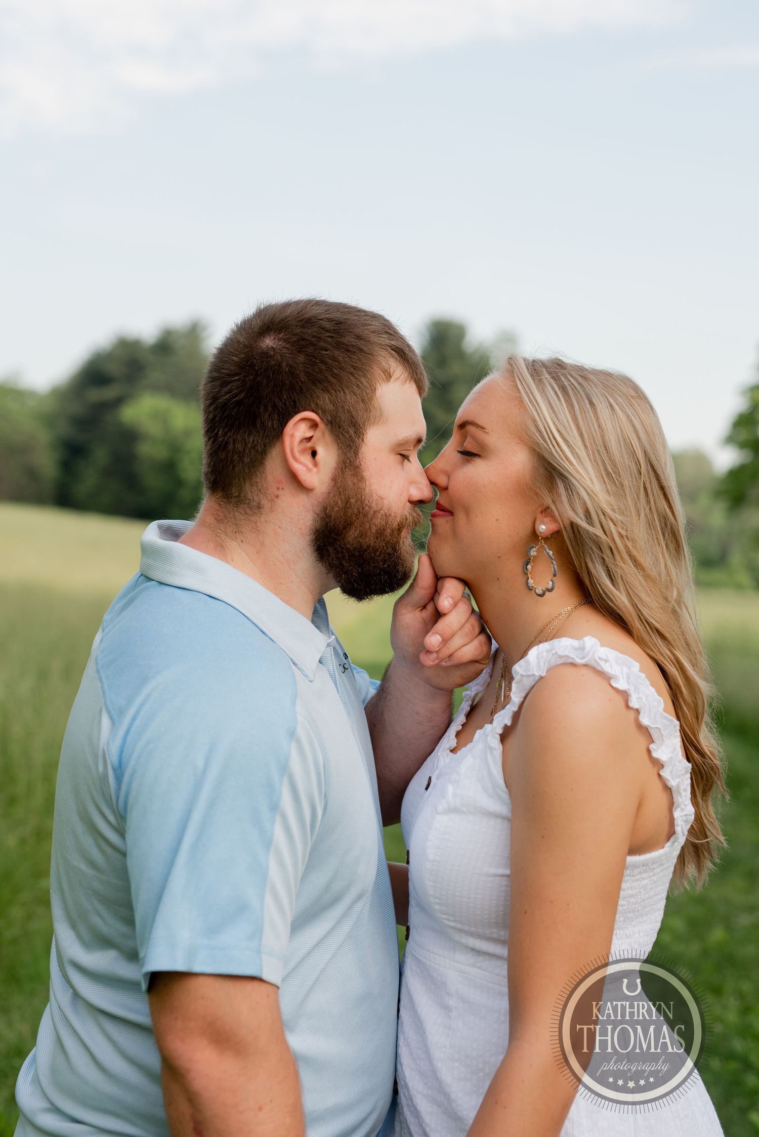 A playful romantic moment between a couple standing close together in a summer field.