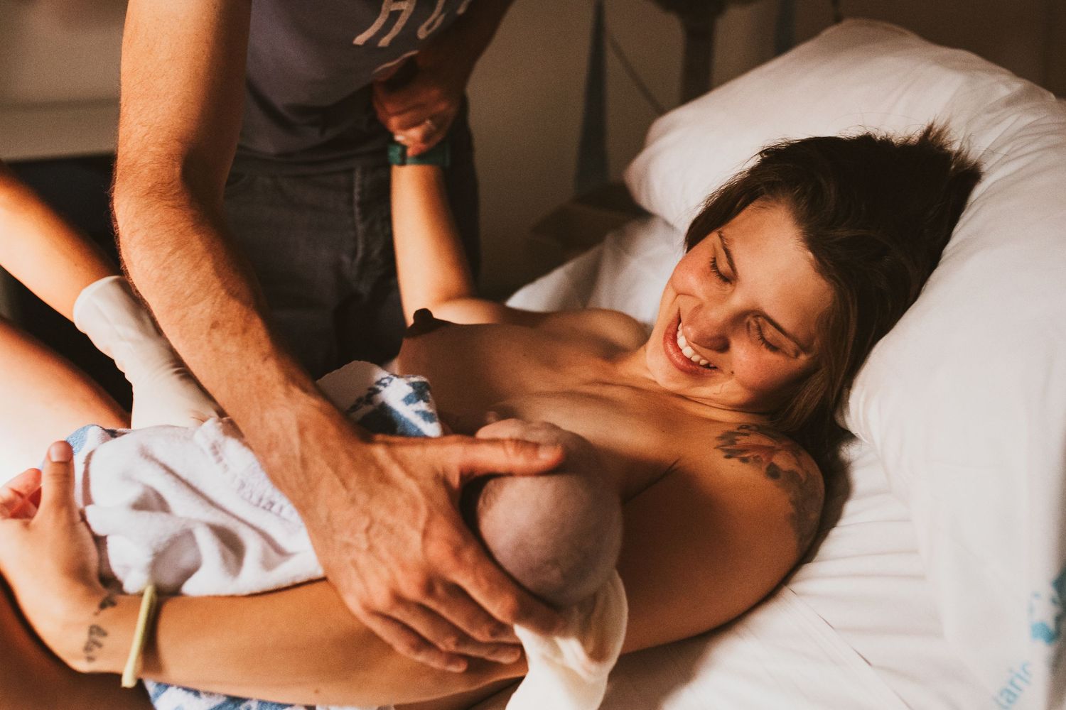 A tender moment during skin-to-skin contact with a newborn baby lying on a white bed.