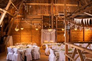 Rustic barn wedding reception with white draped tables, string lights, and bunting decorations in a warm wooden interior.