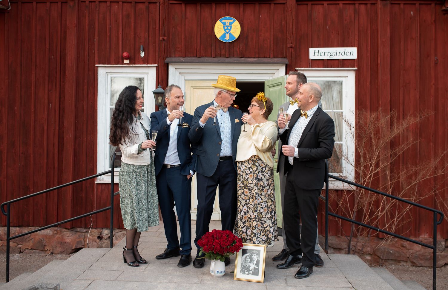Group photo outside red building entrance with decorative elements and formal dress.