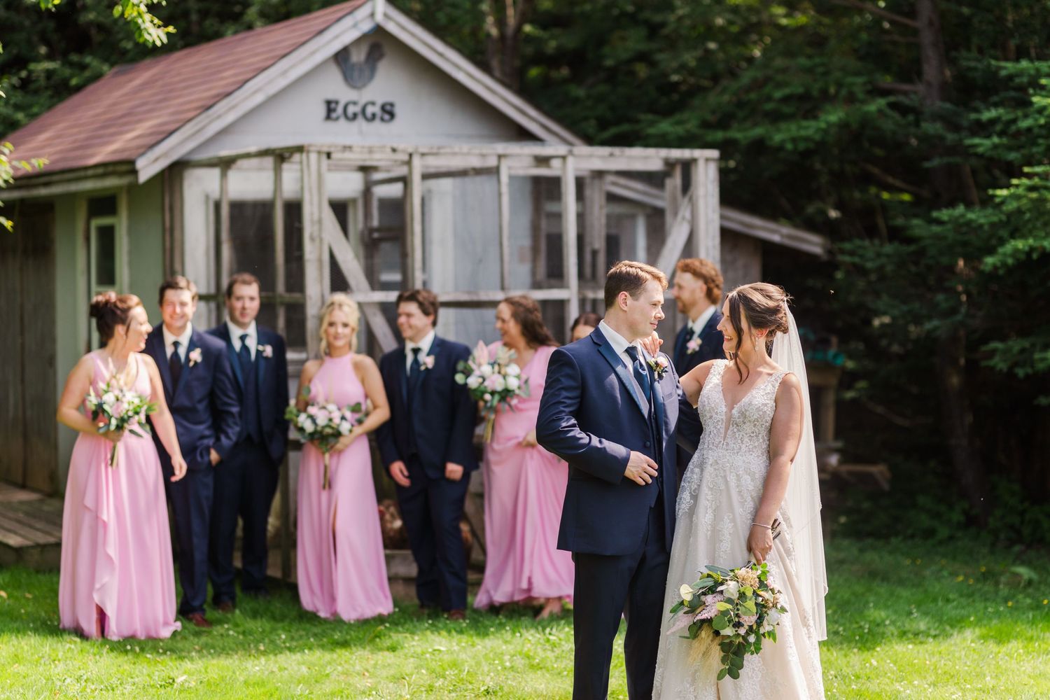A wedding party poses in front of a rustic cabin with bridesmaids in pink dresses.