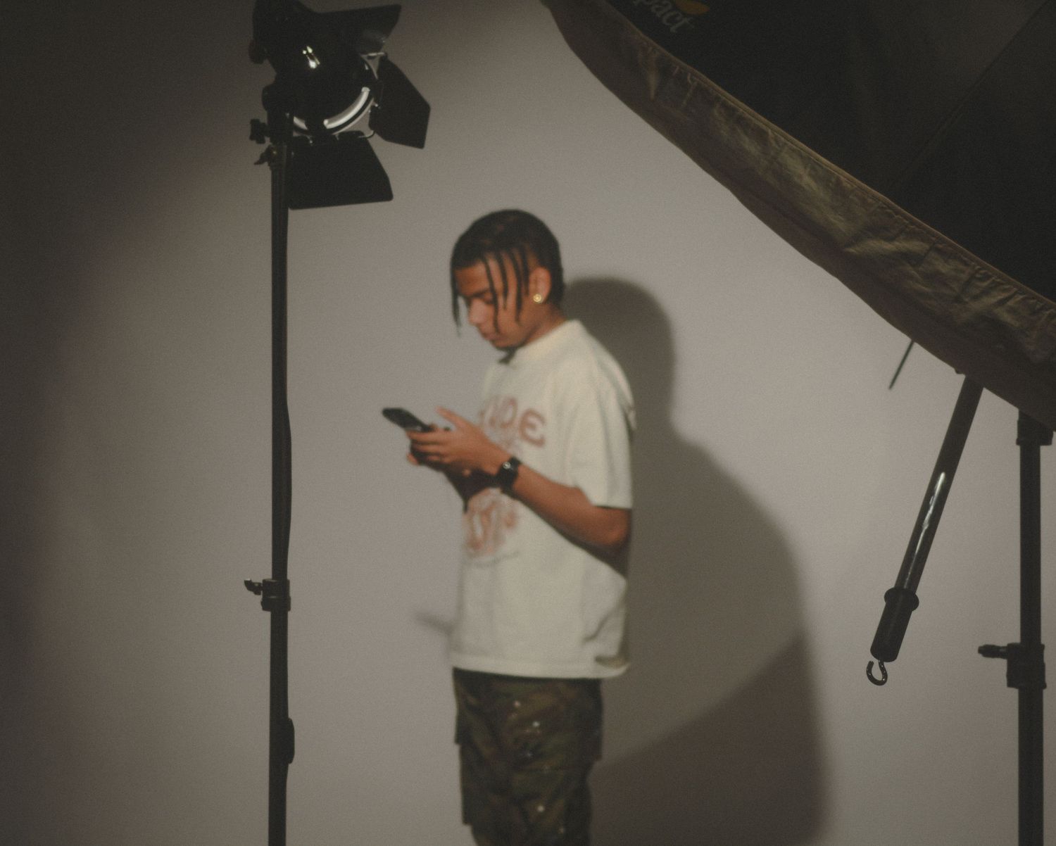 Person in white t-shirt looking at phone in photography studio with lighting equipment.