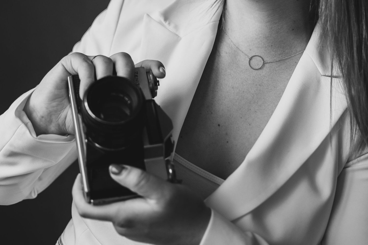 Black and white closeup of hands holding a camera lens while wearing a white blazer.