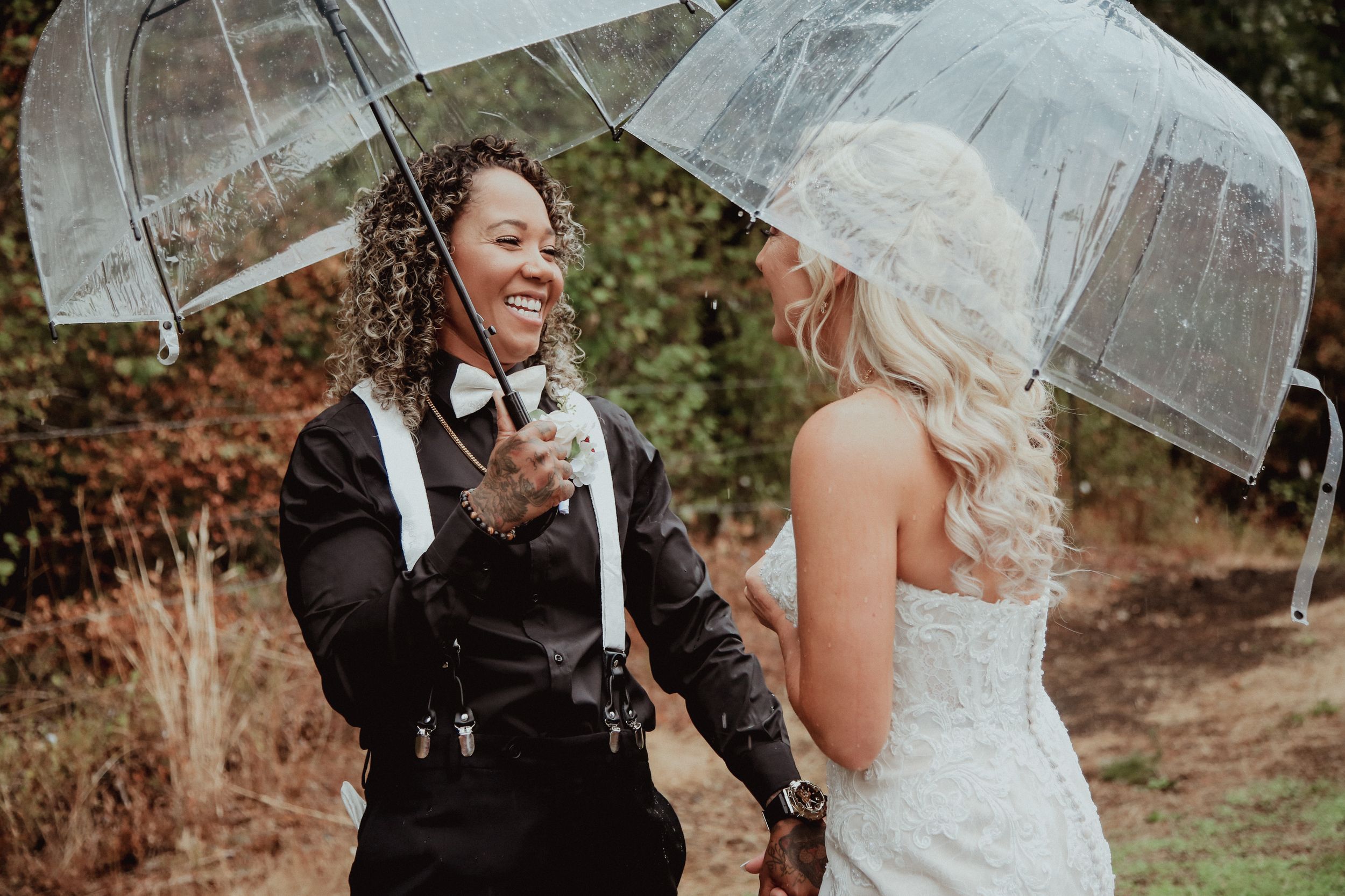 Wedding couple sharing a moment under clear umbrellas in a wooded setting.