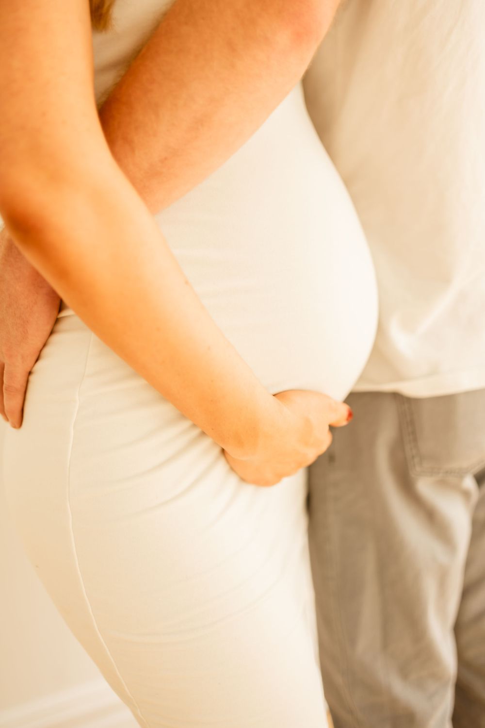 Close-up shots of maternity photos showing pregnant belly in white dress.