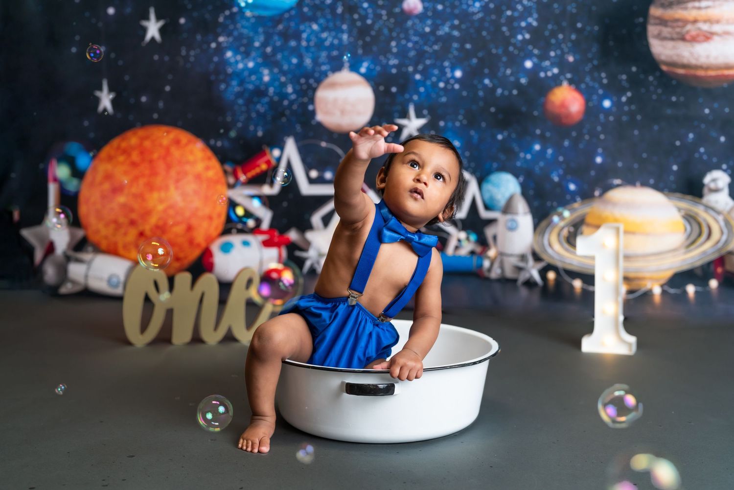 Baby sitting in white basin against cosmic backdrop with planets and stars.