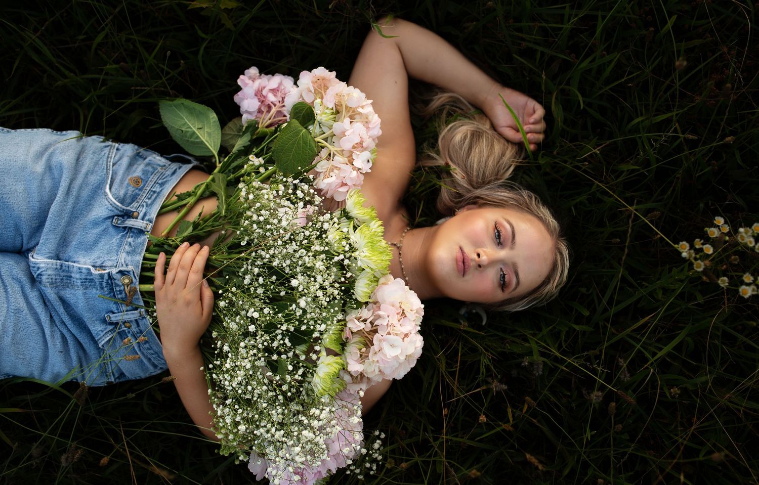 Blonde woman laying in the grass with beautiful flowers covering her