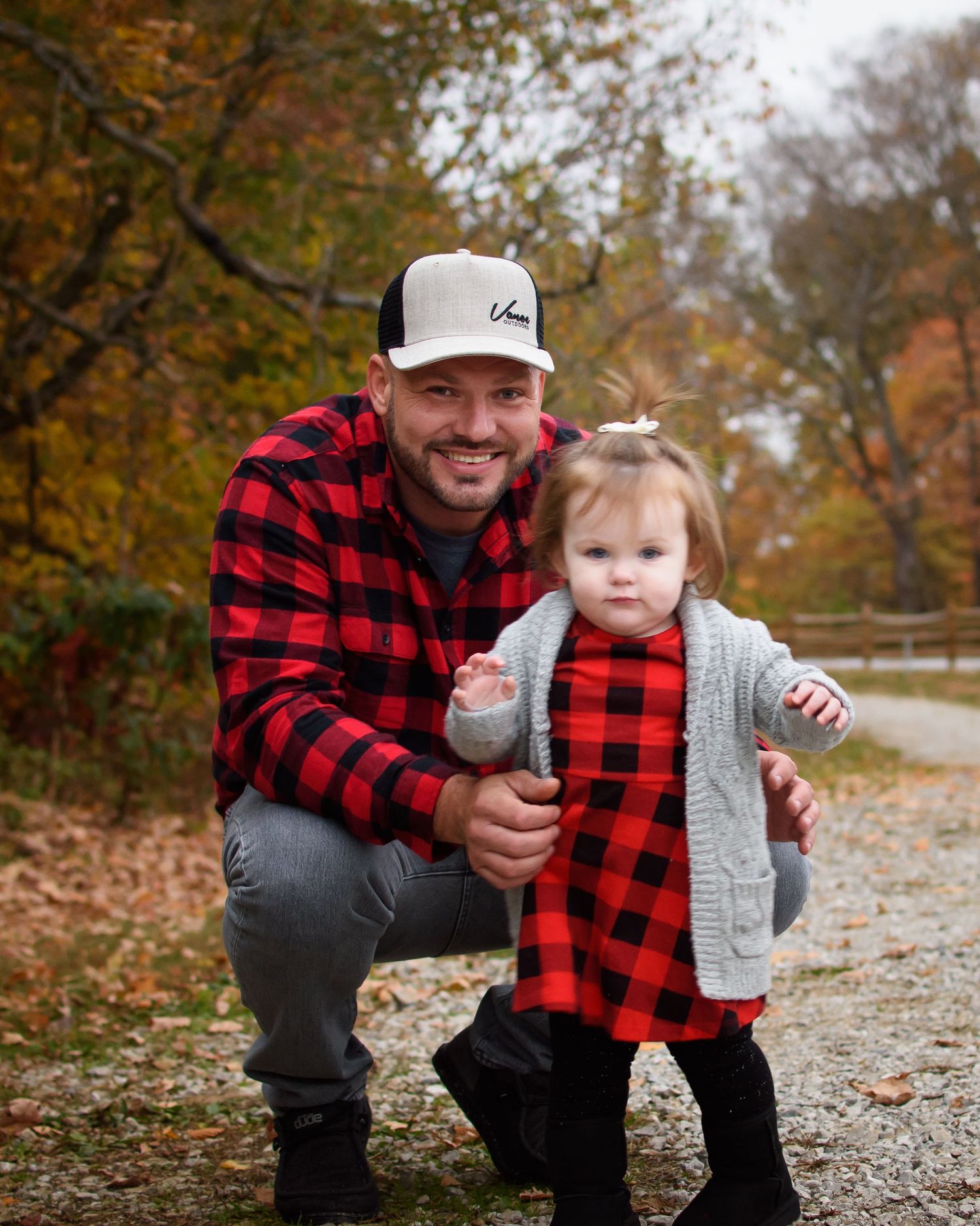 Father and toddler daughter in matching red buffalo plaid outfits posing on a fall nature path.