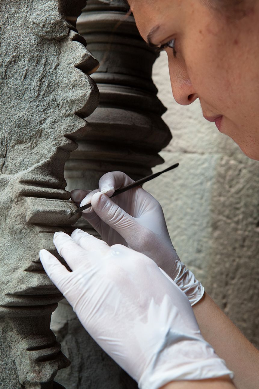 A female conservator works on restoring an ancient balustrade in Angkor Wat. with a small brush.
