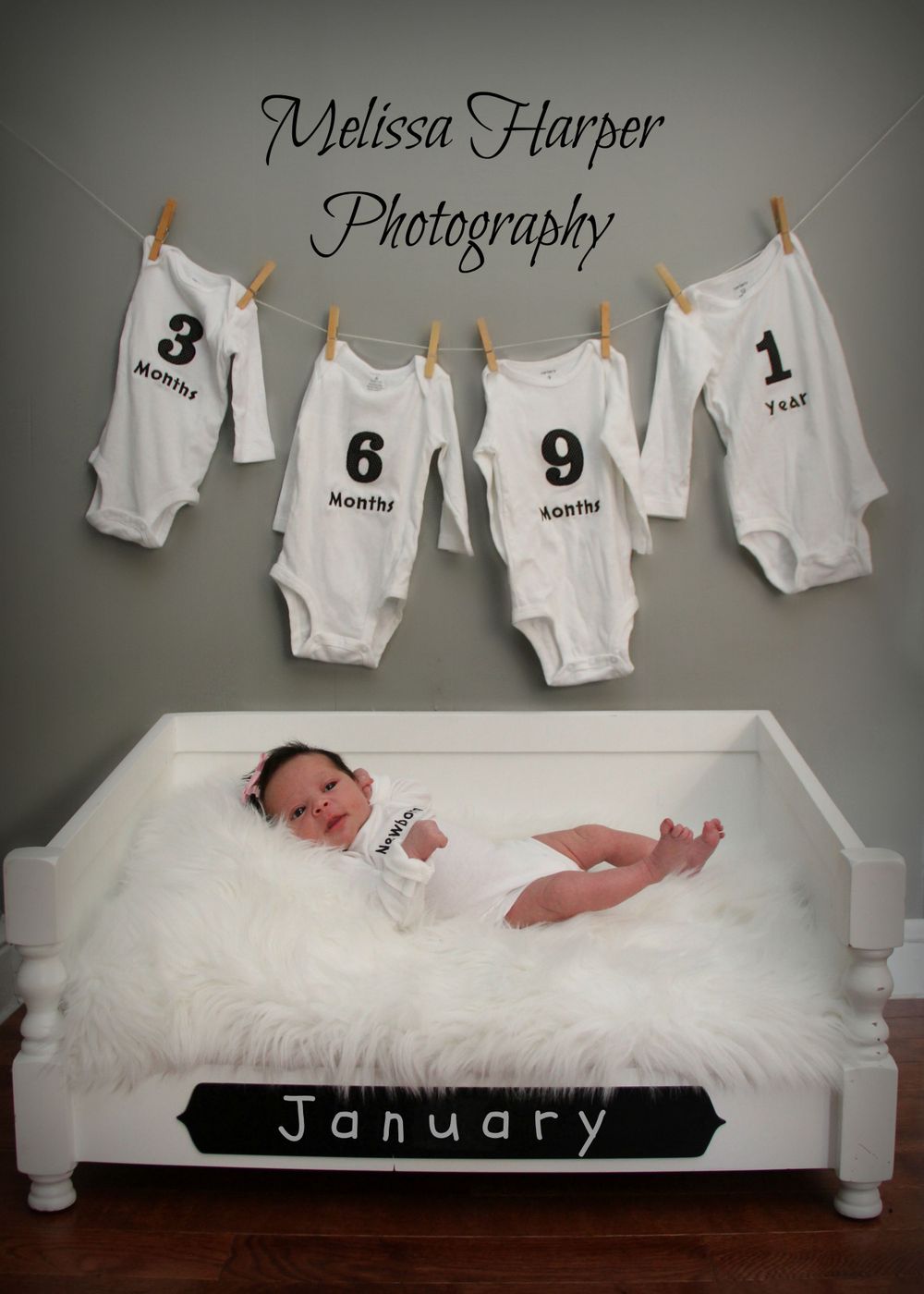 Baby photography setup with numbered onesies 1-9 hanging above white bed with plush fur bedding.