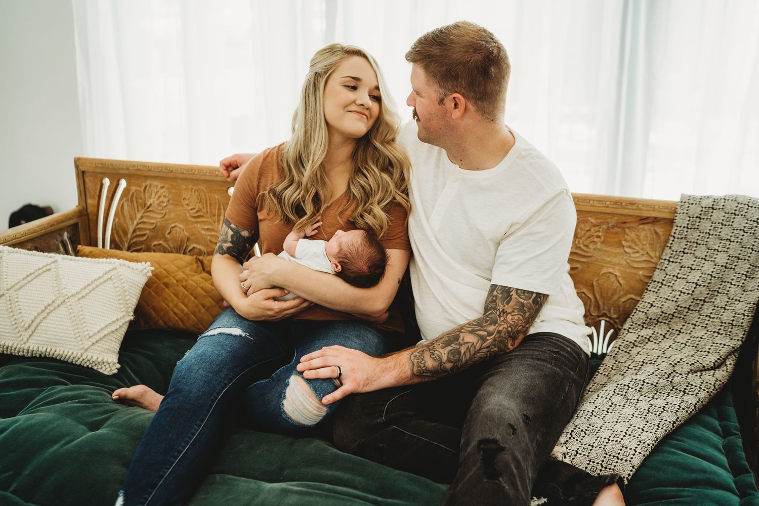 Parents sitting on couch sharing intimate moment with newborn baby on green velvet sofa.